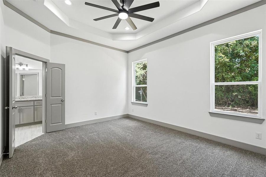 Unfurnished bedroom with a raised ceiling, carpet floors, ensuite bath, a ceiling fan, and recessed lighting Unfurnished bedroom with a raised ceiling, carpet floors, ensuite bath, a ceiling fan, and recessed lighting
