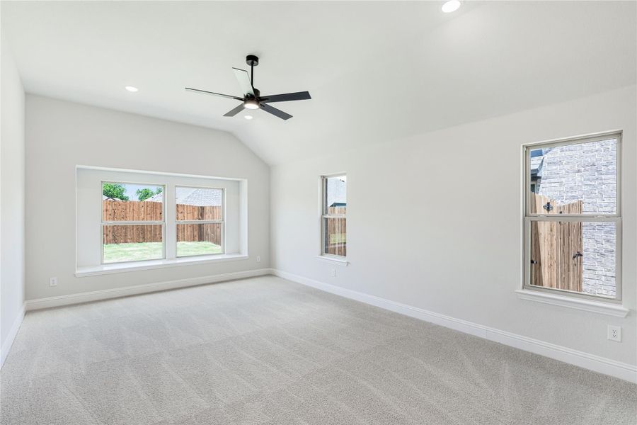 Empty bedroom with vaulted ceiling, ceiling fan, carpet flooring, and multiple windows