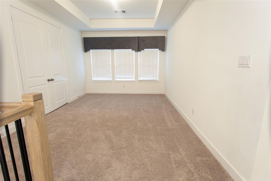 A versatile upstairs game room featuring a tray ceiling, triple windows with designer valances, and plush carpet