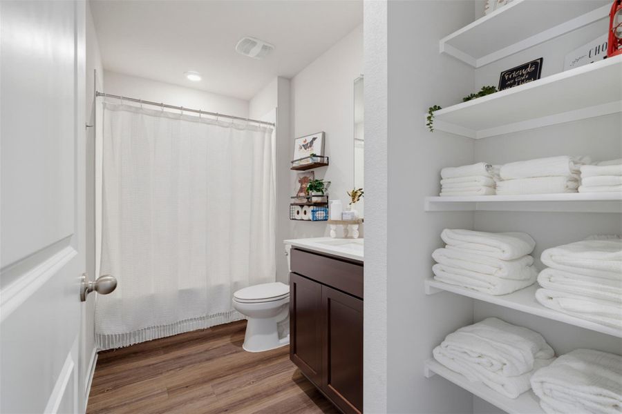 Rich wood-patterned flooring complements a dark wood vanity and built-in linen shelving. Rich wood-patterned flooring complements a dark wood vanity and built-in linen shelving.