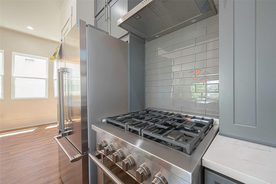 This is a modern kitchen featuring stainless steel appliances, including a gas stove and a large refrigerator, with gray cabinetry and a subway tile backsplash. The room is well-lit with natural light coming from the windows. This is a modern kitchen featuring stainless steel appliances, including a gas stove and a large refrigerator, with gray cabinetry and a subway tile backsplash. The room is well-lit with natural light coming from the windows.