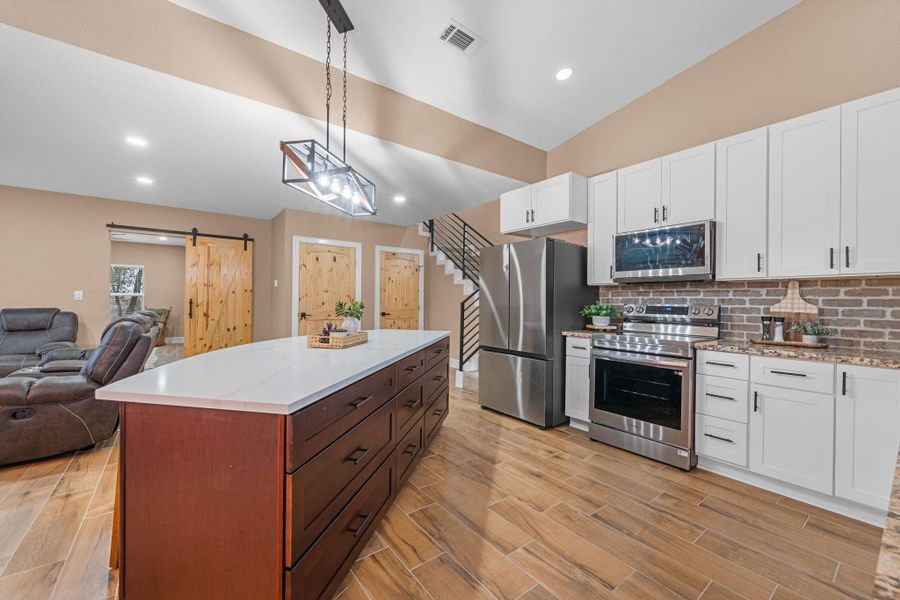 Flows directly into the dining and living areas, highlighted by custom wood doors and a modern horizontal-rail staircase.