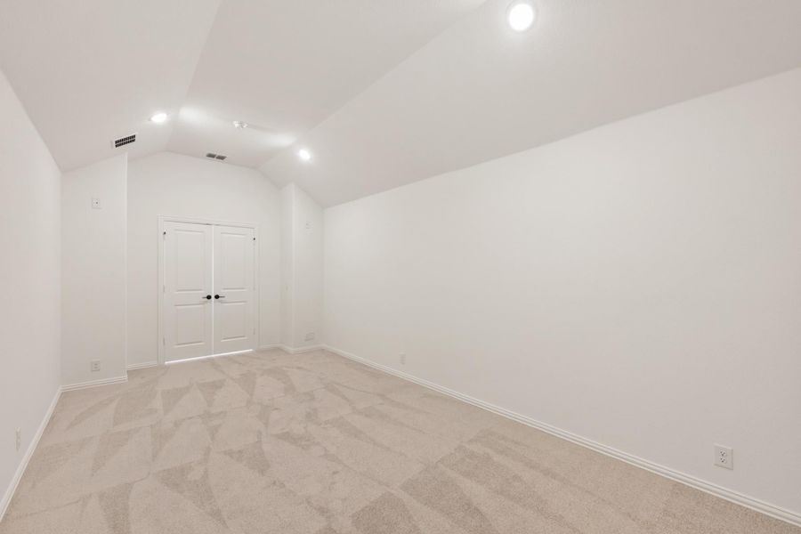 Empty bedroom with vaulted ceiling, recessed lighting, carpet flooring, and double closet doors