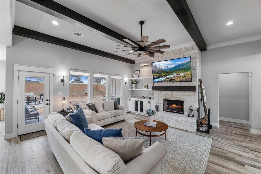 Living room featuring beamed ceiling, ceiling fan, a stone fireplace, and light hardwood / wood-style floors