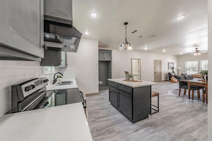 Kitchen with electric range, a breakfast bar area, extractor fan, gray cabinetry, and pendant lighting