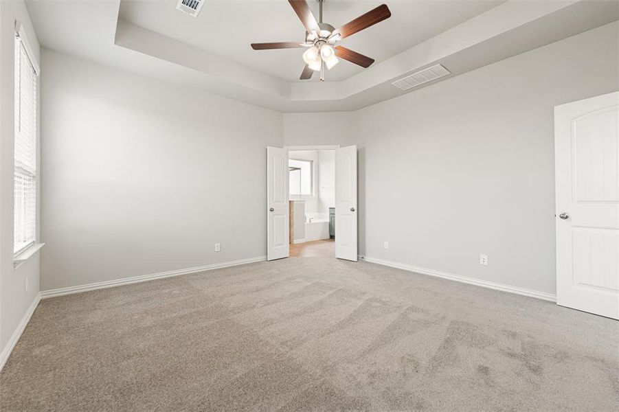 Unfurnished bedroom with a tray ceiling, light colored carpet, and ceiling fan Unfurnished bedroom with a tray ceiling, light colored carpet, and ceiling fan