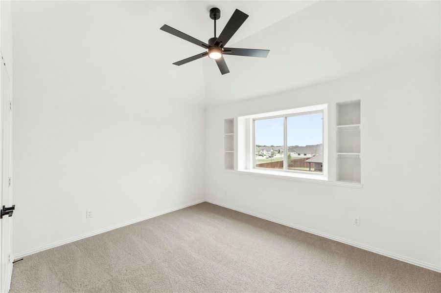 Empty bedroom with vaulted ceiling, black ceiling fan, built-in shelves, and large window with neighborhood view Empty bedroom with vaulted ceiling, black ceiling fan, built-in shelves, and large window with neighborhood view