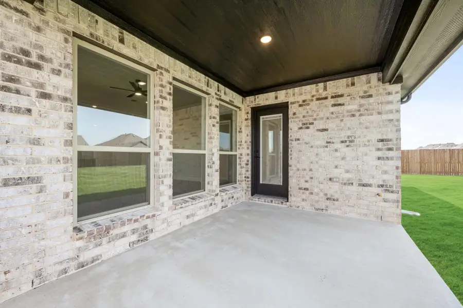 Covered back patio with concrete floor, dark ceiling, and brick exterior wall with black door and windows Covered back patio with concrete floor, dark ceiling, and brick exterior wall with black door and windows