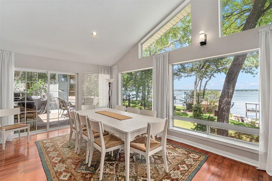 Dining area featuring panoramic windows with water scenery, wood-finish flooring, a vaulted ceiling, and recessed lighting
