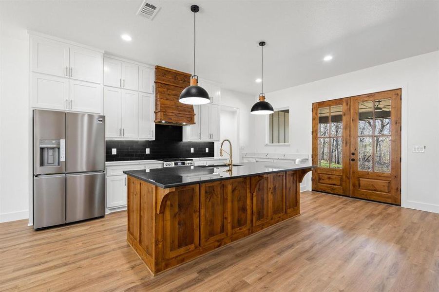 Kitchen featuring white cabinets, an island with sink, pendant lighting, and stainless steel fridge