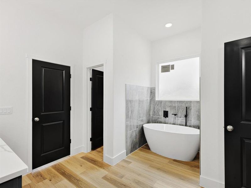 Full bath with a soaking tub, tile walls, vanity, and light wood-style flooring Full bath with a soaking tub, tile walls, vanity, and light wood-style flooring