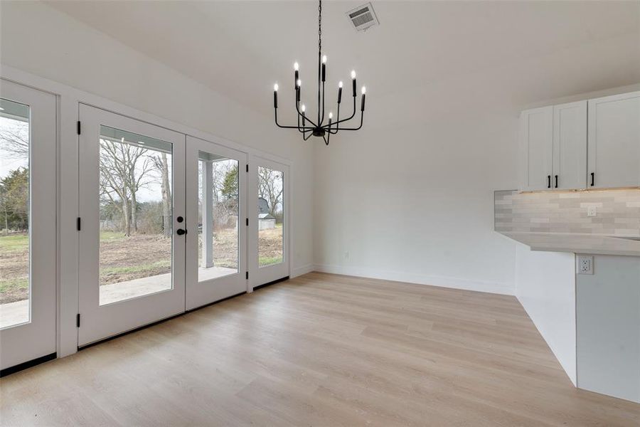 Unfurnished dining area featuring light hardwood / wood-style flooring, french doors, and a chandelier