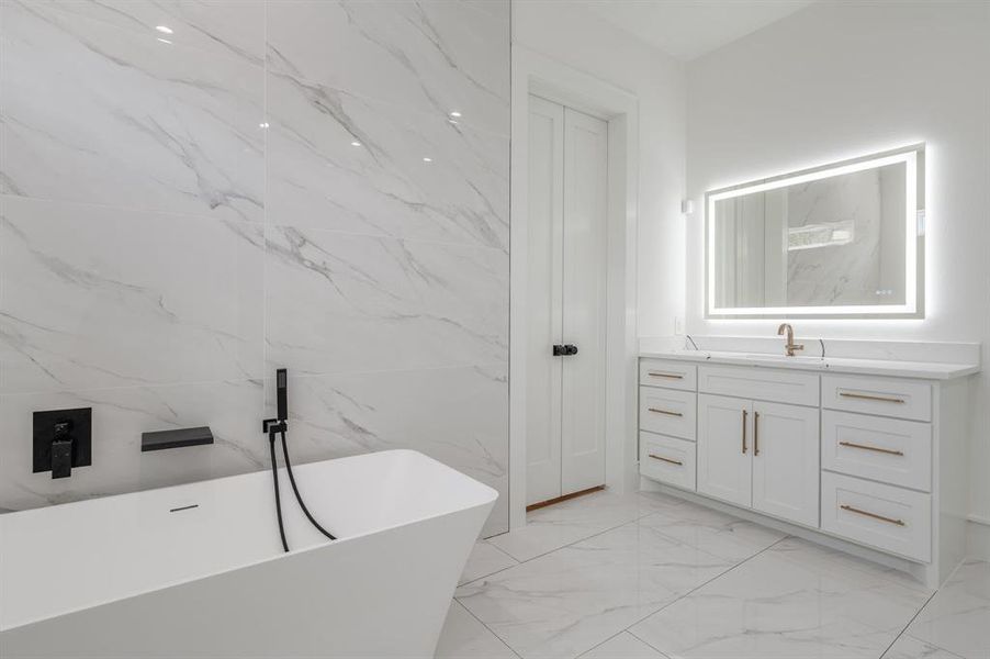 Bathroom featuring vanity, a freestanding tub, light marble finish floors, and stone wall Bathroom featuring vanity, a freestanding tub, light marble finish floors, and stone wall