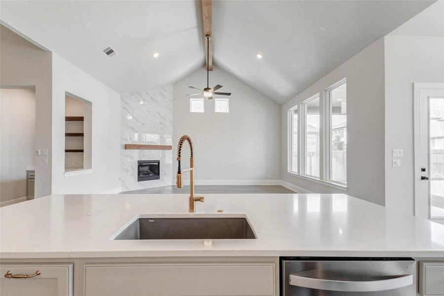 Open-concept living space with high ceilings and a sleek kitchen island. Cozy fireplace with a marble accent wall, large windows for natural light, and a ceiling fan for comfort. Perfect for entertaining and everyday living.
