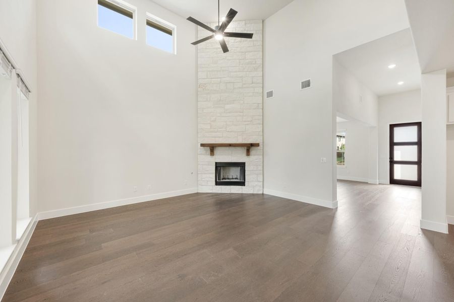 Open living room with soaring ceilings, floor-to-ceiling stone fireplace, ceiling fan, and dark hardwood floors