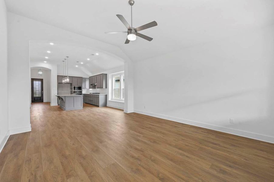 Unfurnished living room with baseboards, wood finished floors, lofted ceiling, and arched walkways