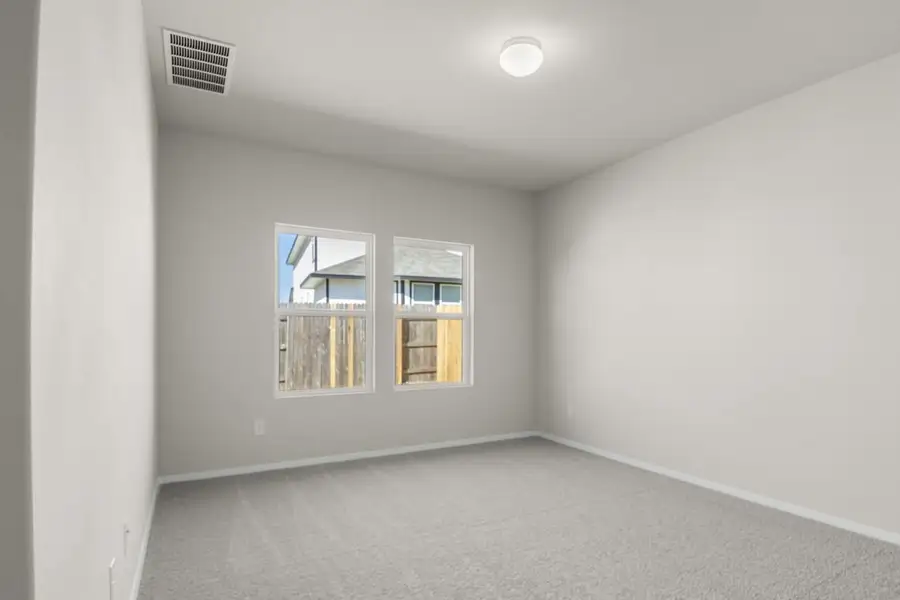 Image of a primary bedroom with cream walls, tan carpeting. two windows and white trim