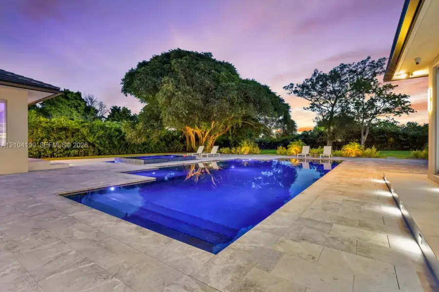 In-ground swimming pool with built-in spa, stone paver patio, and mature tree landscaping