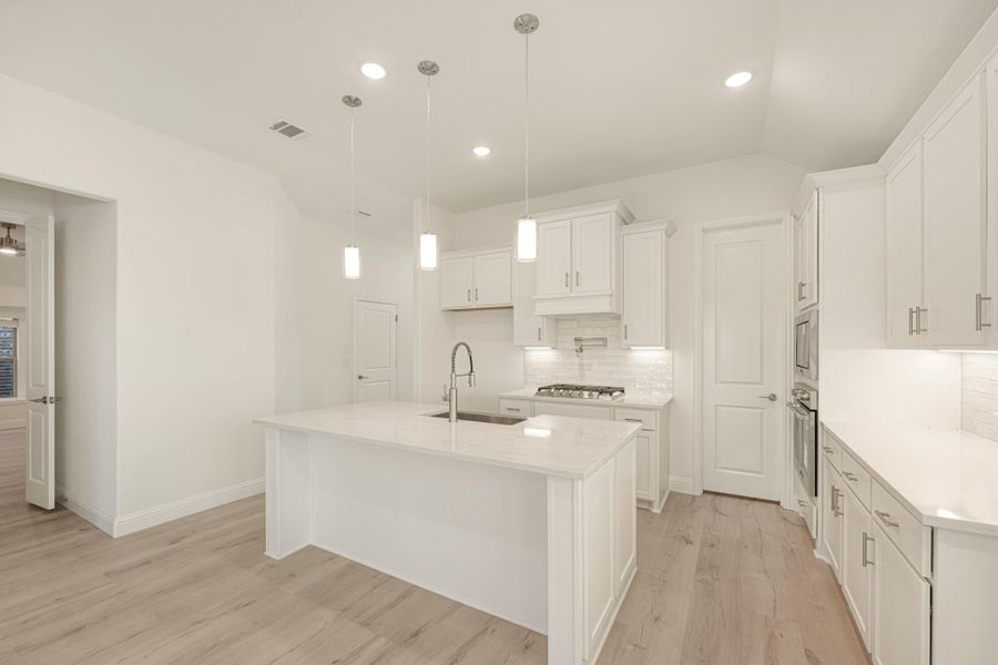 White kitchen with large center island, pendant lights, white cabinets, and light wood floors