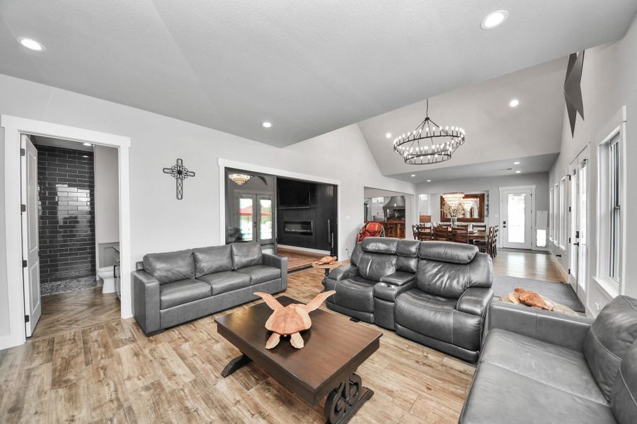 Spacious living area with elegant wood flooring, featuring plush leather seating, a cozy fireplace, and a grand chandelier.