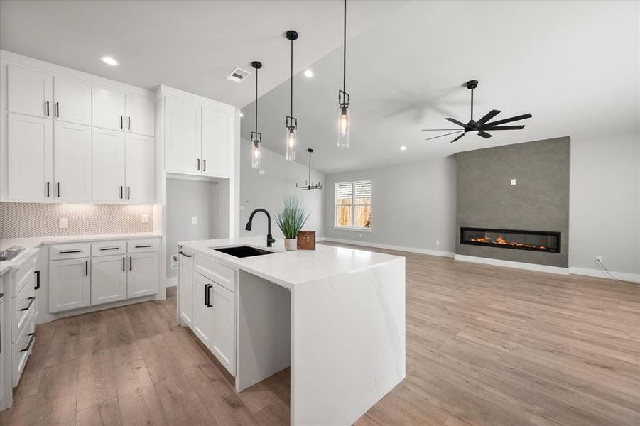 Kitchen featuring decorative backsplash, light stone counters, white cabinets, wood finished floors, and decorative light fixtures Kitchen featuring decorative backsplash, light stone counters, white cabinets, wood finished floors, and decorative light fixtures