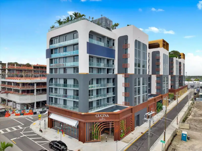 Modern multi-story structure featuring a stucco exterior with tiered balconies, glass railings, metal-slat design elements, and a ground-level commercial storefront
