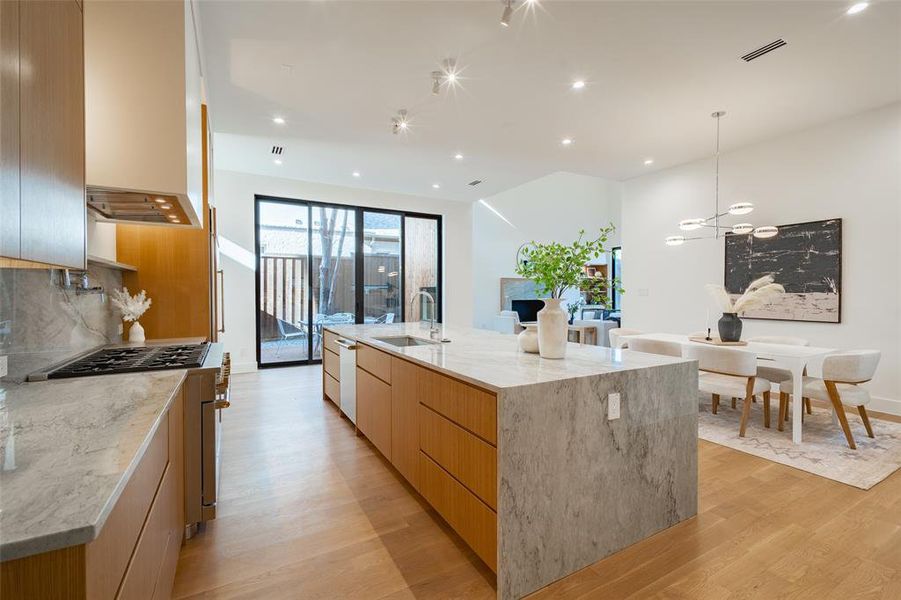 Kitchen with pendant lighting, sink, a large island with sink, light stone countertops, and light hardwood / wood-style flooring