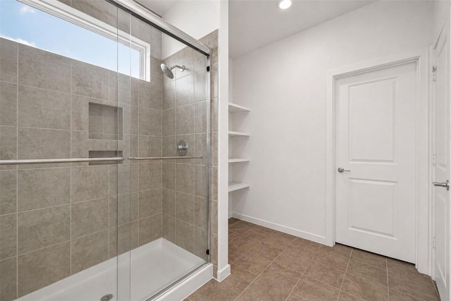 Primary bathroom featuring a spacious walk-in shower with tile surround, built-in shower niche, and natural light. Direct access to the primary closet for added convenience and functionality. Clean, bright layout with additional built-in storage shelving.