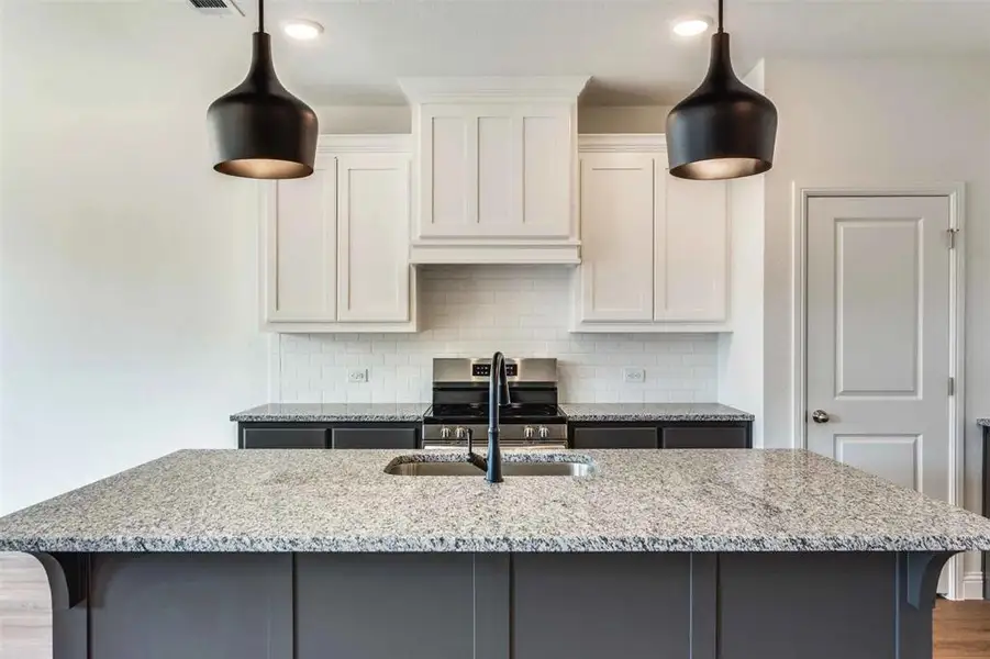 Kitchen with light stone countertops, stainless steel range, a kitchen island with sink, backsplash, and recessed lighting
