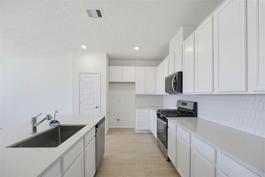 The kitchen features high ceilings, stained wood cabinets, Silestone countertops, SS appliances including microwave, modern tile backsplash, recessed lighting, huge kitchen island extended for a breakfast bar, and a pantry all overlooking your huge family room.