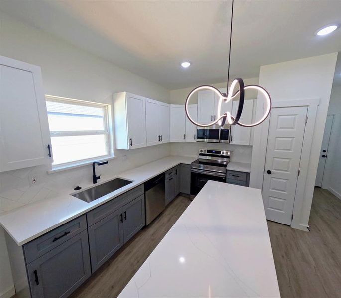 Kitchen with gray cabinetry, white cabinets, appliances with stainless steel finishes, backsplash, and recessed lighting Kitchen with gray cabinetry, white cabinets, appliances with stainless steel finishes, backsplash, and recessed lighting