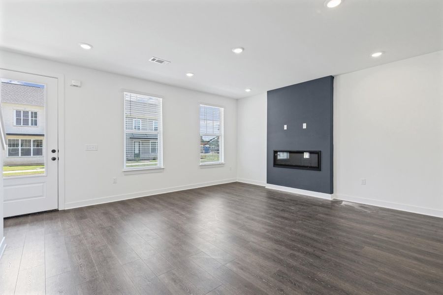 Wood-finish flooring, recessed lighting, and a modern linear fireplace with a contrasting accent wall