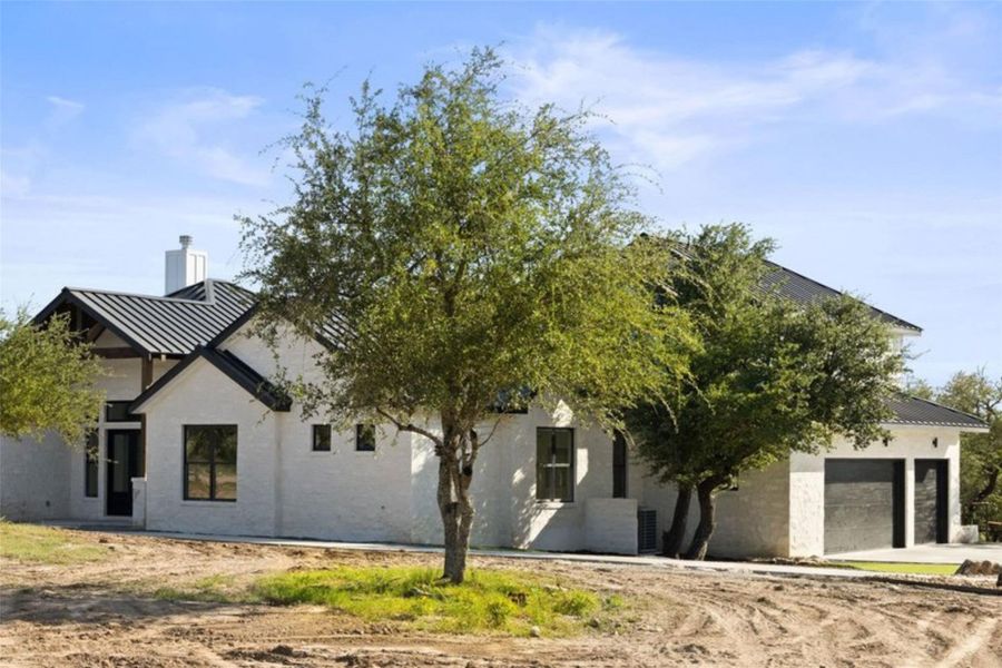 A newly constructed residence features modern design with clean lines and mature trees framing the entry. A newly constructed residence features modern design with clean lines and mature trees framing the entry.