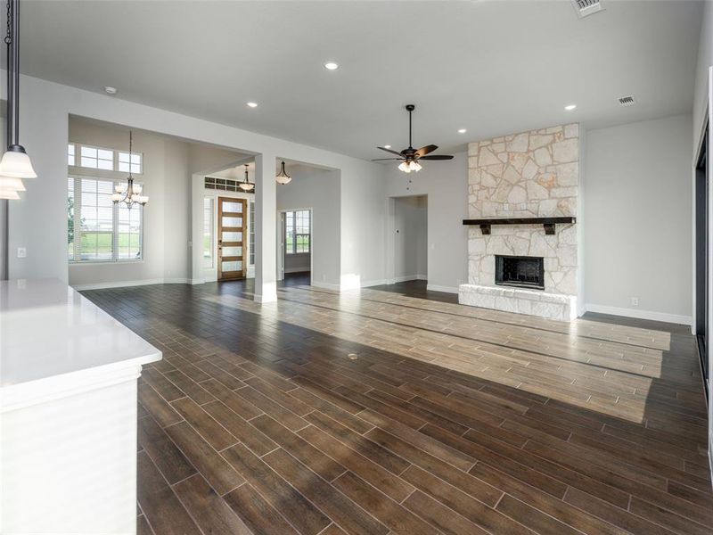 Unfurnished living room featuring a ceiling fan, recessed lighting, dark wood-style floors, a stone fireplace, and a chandelier