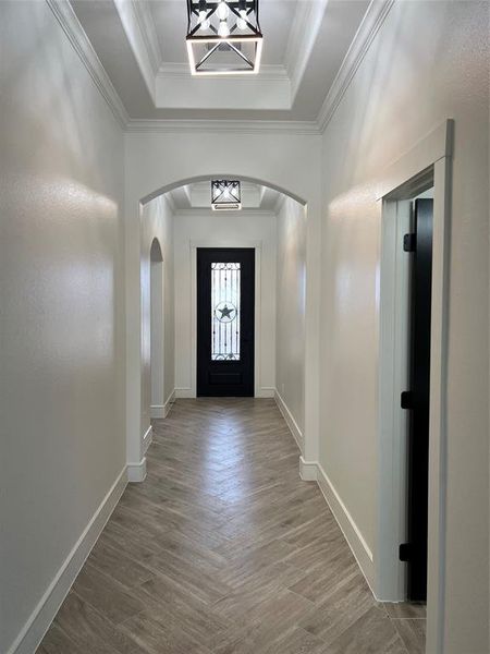 Foyer with arched walkways, light wood-type flooring, crown molding, and a tray ceiling