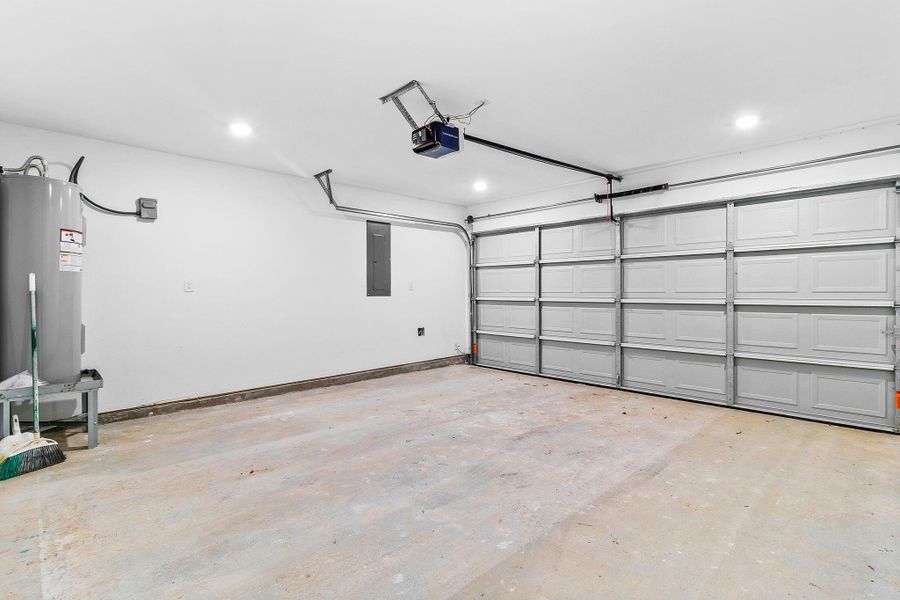 This spacious garage features a double-door entry, clean white walls, and a water heater in the corner. It has ample lighting and room for multiple vehicles or storage.