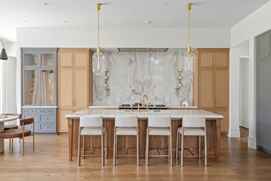 An expansive natural stone island takes center stage in the kitchen, complemented by custom white oak cabinetry, warm brass details, and a dramatic full-height stone backsplash. Thoughtfully layered materials give the space a refined, collected feel while maintaining the warmth that carries throughout the home. An expansive natural stone island takes center stage in the kitchen, complemented by custom white oak cabinetry, warm brass details, and a dramatic full-height stone backsplash. Thoughtfully layered materials give the space a refined, collected feel while maintaining the warmth that carries throughout the home.
