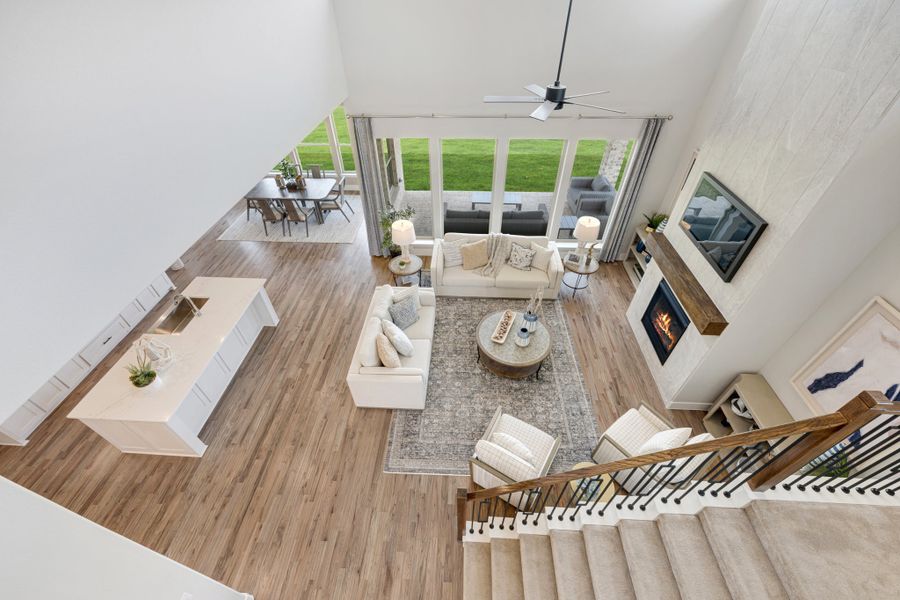 Open-concept living area with two-story ceiling, fireplace, hardwood floors, and large windows viewed from above.