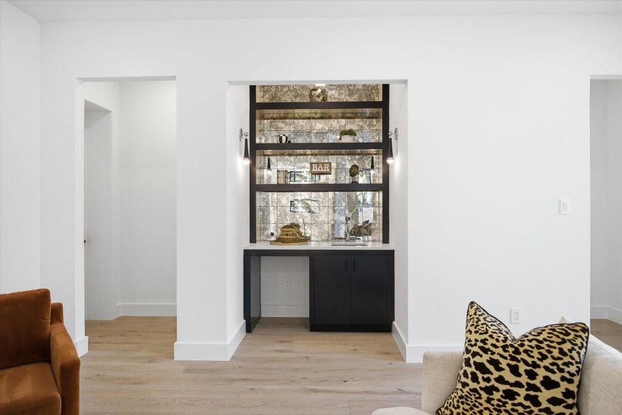 A custom-built bar area serves as the focal point, complete with designer shelving, accent lighting, and a striking backsplash that adds depth and texture.