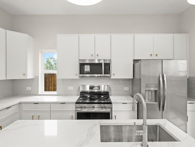 Contemporary kitchen featuring white cabinetry, stainless steel appliances, light-toned countertops, a subway tile backsplash, and an integrated kitchen island sink