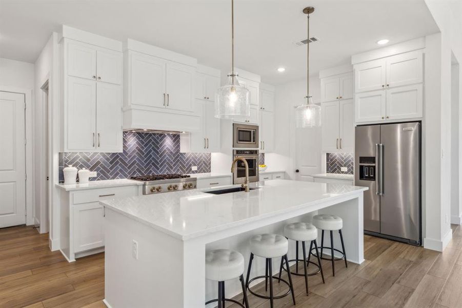 Kitchen featuring appliances with stainless steel finishes, light hardwood / wood-style flooring, backsplash, and an island with sink