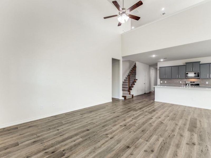 Unfurnished living room with light wood-style floors, a high ceiling, stairway, and ceiling fan