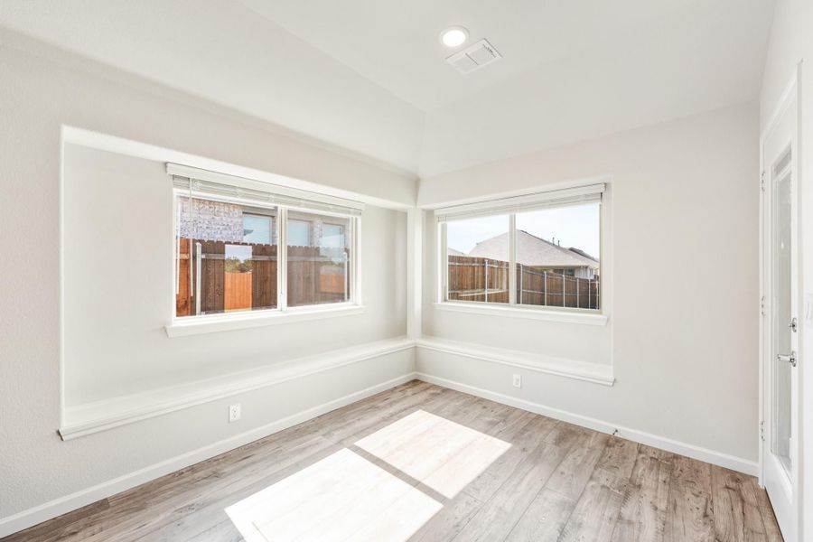 Empty room with light wood floors, white walls, and two corner windows with backyard views