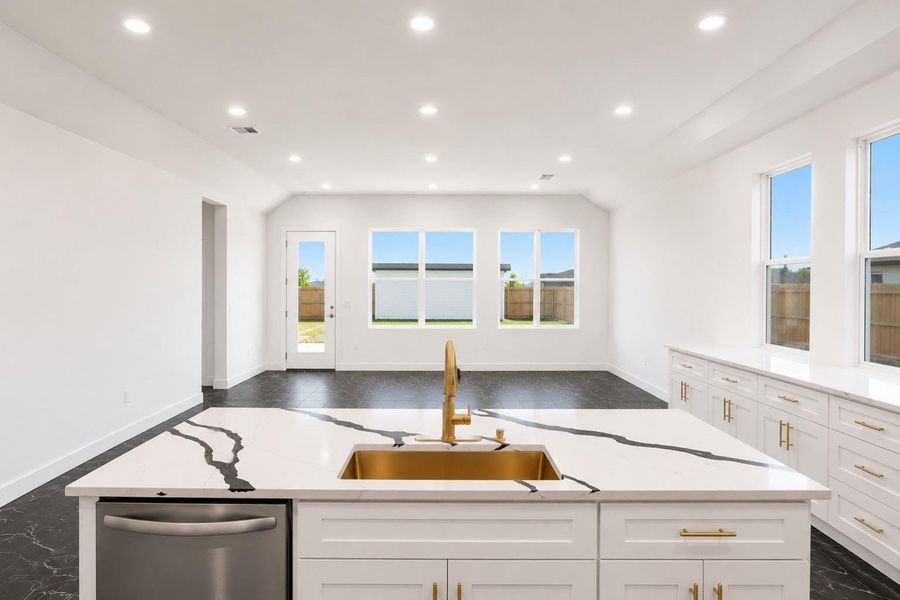 A well-lit kitchen boasts a pristine island with a gold sink, set against a backdrop of ample windows and a glass-paneled door.
