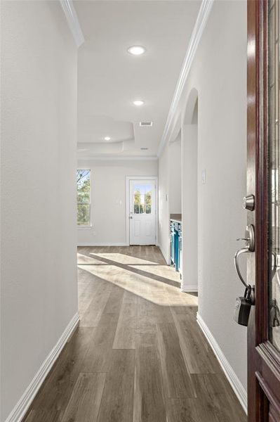 Hallway with wood finished floors, ornamental molding, recessed lighting, a raised ceiling, and arched walkways