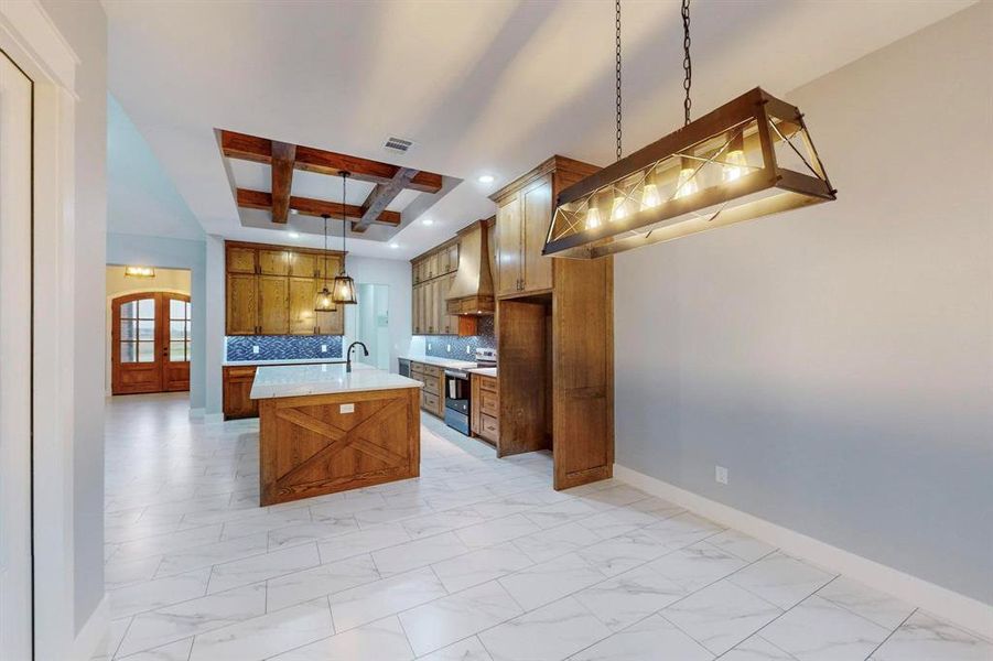 Kitchen featuring beamed ceiling, decorative light fixtures, stainless steel electric range, a kitchen island with sink, and premium range hood