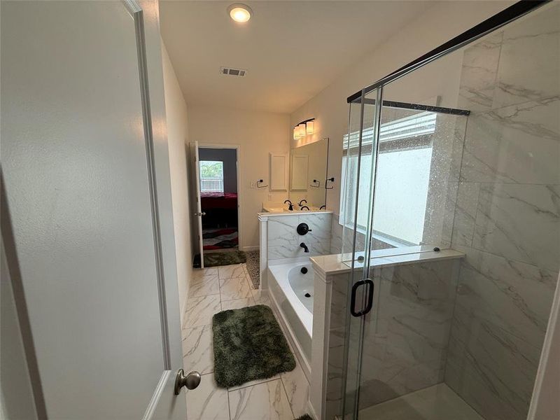 Bathroom featuring a glass-enclosed shower with marble-look tile, a separate built-in soaking tub, dual vanity with undermount sinks, and marble-look tile flooring