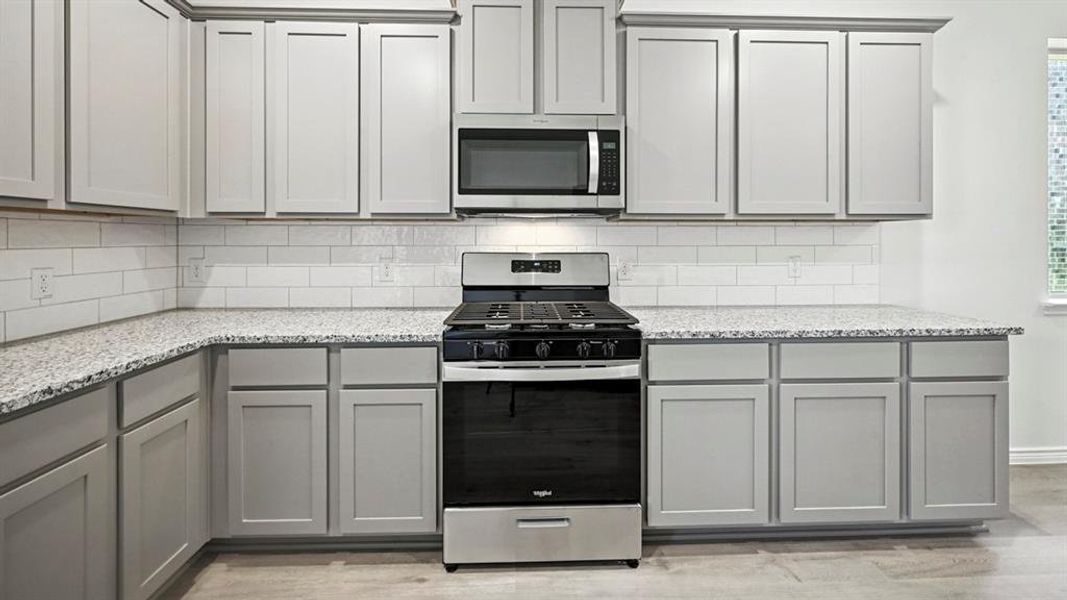 Kitchen with gray cabinets, stainless steel appliances, light stone countertops, tasteful backsplash, and light wood-style floors Kitchen with gray cabinets, stainless steel appliances, light stone countertops, tasteful backsplash, and light wood-style floors