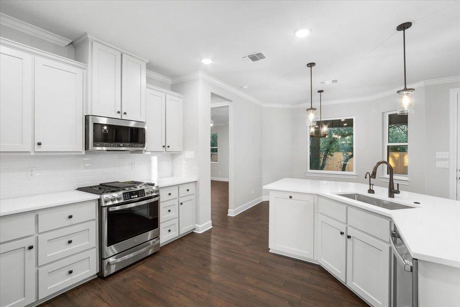 Kitchen with appliances with stainless steel finishes, a sink, dark wood-style floors, backsplash, and light countertops Kitchen with appliances with stainless steel finishes, a sink, dark wood-style floors, backsplash, and light countertops