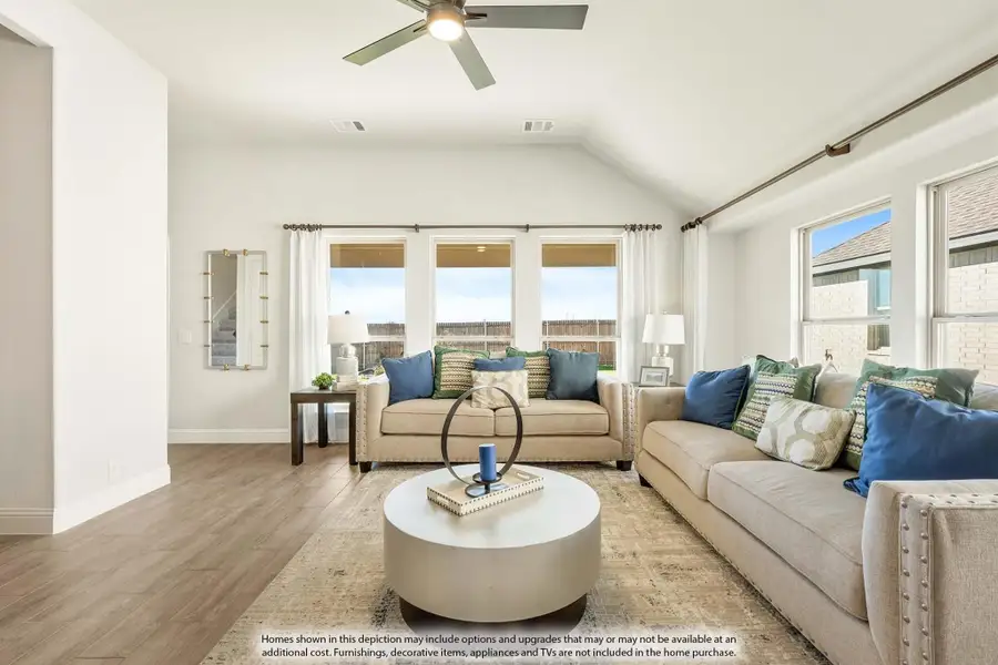 Living room with vaulted ceiling, ceiling fan, hardwood floors, and two beige sofas with blue accent pillows